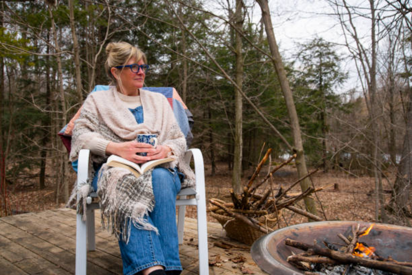 a woman sitting in a chair with a mug of coffee and a fire pit